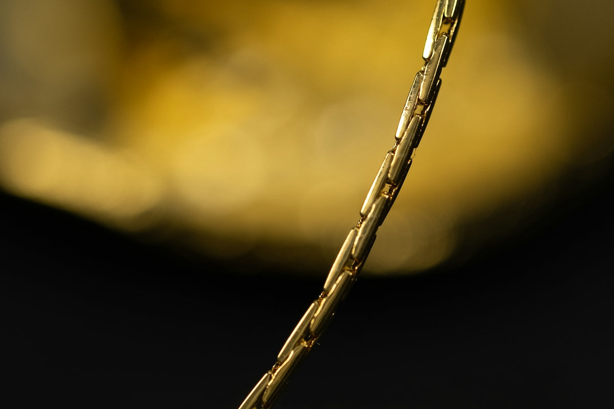 A gold chain link necklace against a dark background with golden bokeh